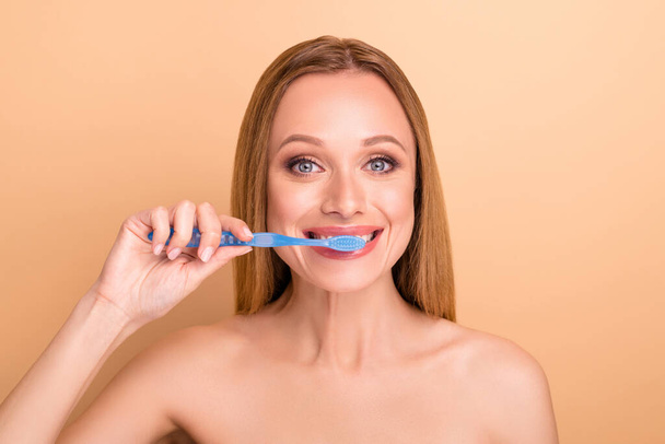 Close-up view portrait of nice-looking attractive cheerful cheery nude naked girl brushing white teeth everyday effective anti caries treatment isolated on beige pastel background - Фото, изображение