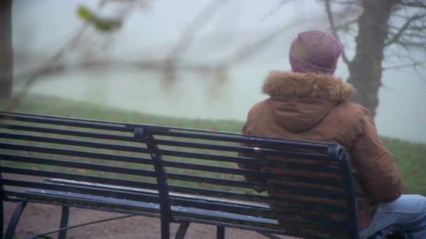 Osamělý stařec sedí na lavičce a dívá se v zimním ránu do mlhy. - Záběry, video