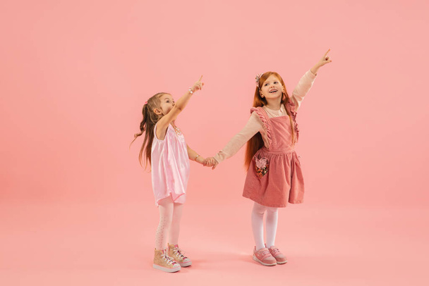 Childhood and dream about big and famous future. Pretty little girls isolated on coral pink background - Zdjęcie, obraz