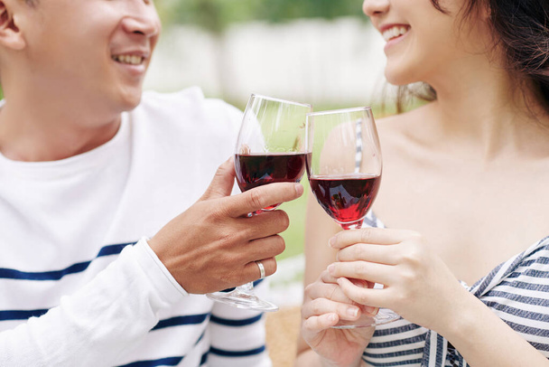 Açık havada romantik bir buluşma yaşarken gülümseyen sevgili ve kız arkadaşın kırmızı şarap içerkenki yakın plan görüntüsü. - Fotoğraf, Görsel