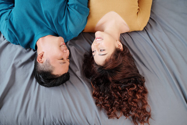 Весела молода азіатська пара лежить на ліжку і дивиться один на одного. - Фото, зображення