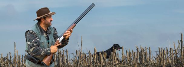 Un cacciatore con una pistola in mano in abiti da caccia nella foresta autunnale in cerca di un trofeo. Un uomo sta con armi e cani da caccia a rintracciare il gioco. - Foto, immagini