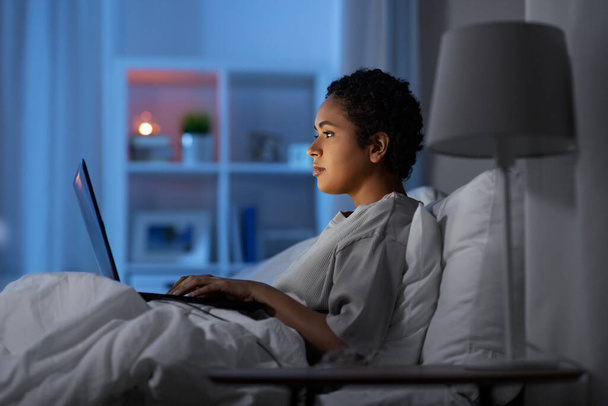woman with laptop in bed at home at night - 写真・画像