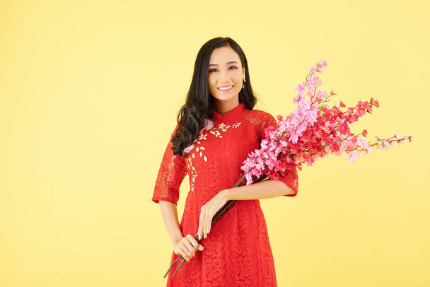 Portrait of young beautiful smiling Asian woman holding bouquet of blooming peach branches - Фото, изображение