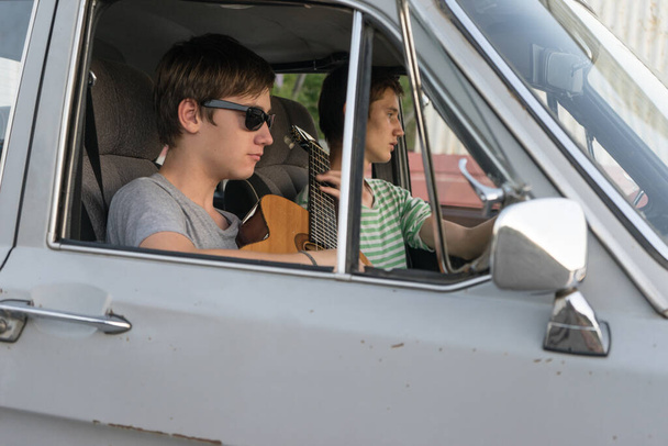 Two young man in the car. boy plays the guitar in the car. cheerful company of young people. journey together. fun pastime. - Fotografie, Obrázek