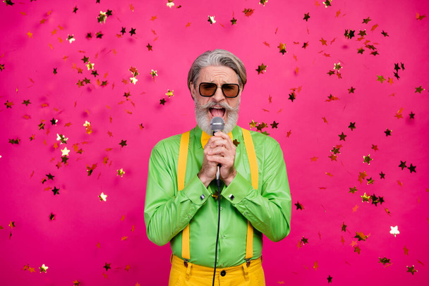 Foto de engraçado vovô clubber festa frio cantando karaoke microfone confete queda regozijando-se desgaste sol especificações verde camisa amarelo suspensórios gravata isolado brilho cor-de-rosa fundo - Foto, Imagem