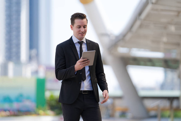 Бизнесмен, стоящий с помощью цифрового планшета перед современными офисными зданиями - Фото, изображение