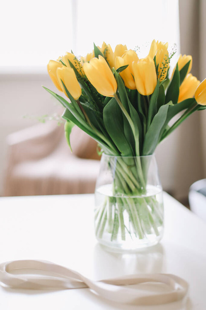Figure eight of beige ribbon with beautiful yellow tulips in a vase. International Women Day, 8 March concept. Flowers illuminating yellow color of the year 2021 - Photo, image