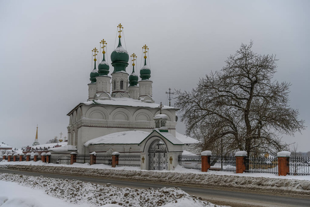 Mírná zima v provinčním městě Solikamsk (Severní Ural, Rusko) Zasněžené ulice a stromy za studeného oblačného dne. Foto dekorace - starý bílý-kámen kostel s mnoha kopulemi  - Fotografie, Obrázek