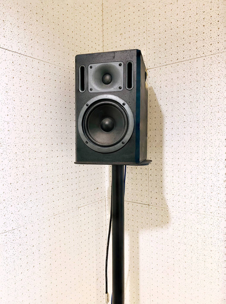 Monitor studyjny, wysokiej jakości głośnik na stalowym stojaku z tablicą akustyczną, ściana pochłaniająca dźwięk jako białe tło. - Zdjęcie, obraz