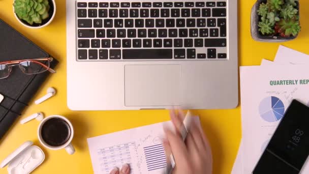 Escritório moderno secretária amarela e mãos de mulher de negócios escrevendo sobre relatório e digitação no laptop vista superior - Filmagem, Vídeo