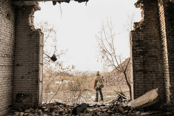 wandering boy. boy with a gun. boy goes to an abandoned building. boy stands in front of a building. Post apocalypse. Boy traveling on foot in a post-apocalyptic world in search of food. - Photo, image