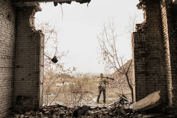 wandering boy. boy with a gun. boy goes to an abandoned building. boy stands in front of a building. Post apocalypse. Boy traveling on foot in a post-apocalyptic world in search of food. - 写真・画像