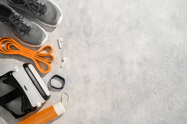 Fitness, workout, and VR technology concept. Sports equipment on grey background: virtual reality glasses, expander, fitness tracker, sneakers, juice. Knolling flat lay composition, copy space - Photo, Image