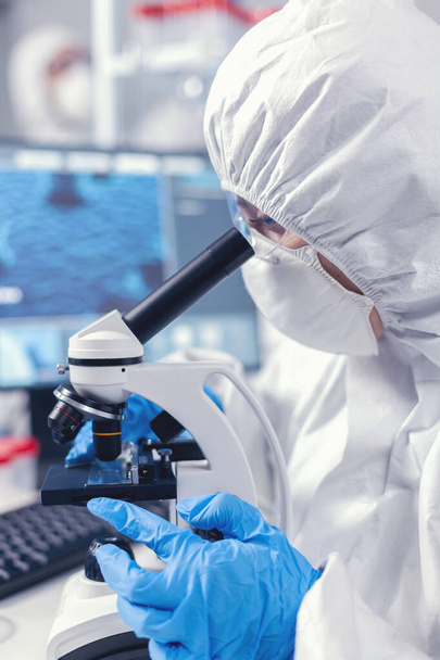 Medical scientist analysing sample on glass slide looking through microscope - Foto, afbeelding