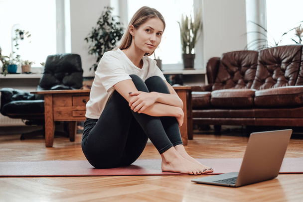 Cheerful sportswoman uses her laptop sitting on floor in modern room - Photo, Image