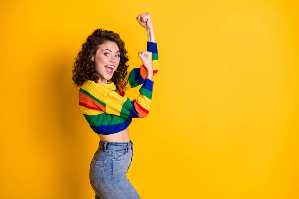 Profile photo of pretty young girl raise fists open mouth wear striped cropped pullover jeans isolated yellow color background - Foto, Imagen