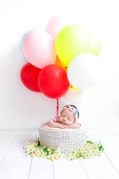 Novorozené dítě spí v koši sedmikrásek. Dítě s barevnými koulemi. Sladký zdravý spánek vašeho dítěte. Dívka letí horkovzdušným balónem. - Fotografie, Obrázek