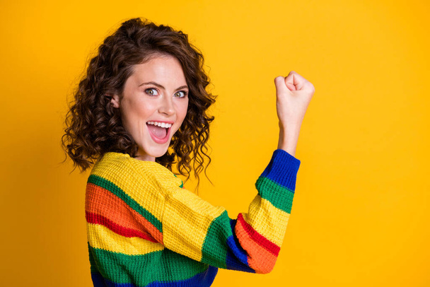 Photo of excited cute lady raise fist open mouth astonished expression wear striped sweater isolated yellow color background - Zdjęcie, obraz