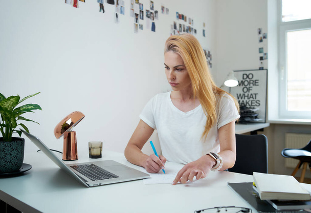 Жінка-фрілансер пише документ з олівцем, сидячи за столом
 - Фото, зображення