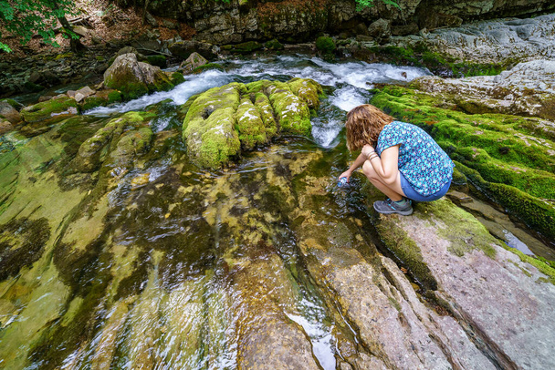 Woman catching water from a clean water river in the mountains. Beauty and ecology in a place without pollution - Fotoğraf, Görsel