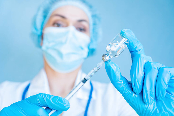 Una doctora sostiene una jeringa y una vacuna en sus manos sobre un fondo azul. Concepto de vacunación e inmunización de la población. Vacunación contra la rubéola y el virus del papiloma humano.  - Foto, Imagen