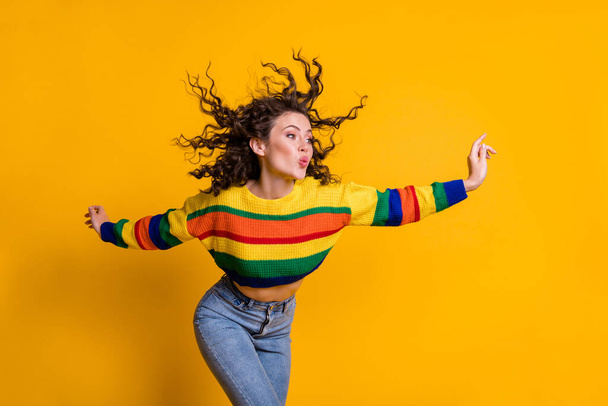 Photo of childish lady wearing casual colorful sweater dancing looking pointing empty space lips pouted isolated yellow color background - Фото, изображение