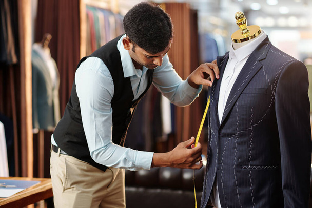 Jeune tailleur créatif mesurant veste sur mesure sur mannequin sur lequel il travaille - Photo, image