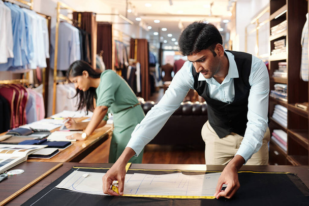 Concentrado joven sastre indio que mide el patrón de costura de la chaqueta para el cliente - Foto, imagen