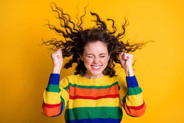 Photo of cheerful lucky lady wearing casual colorful sweater raising fists closed eyes isolated yellow color background - Foto, Imagem