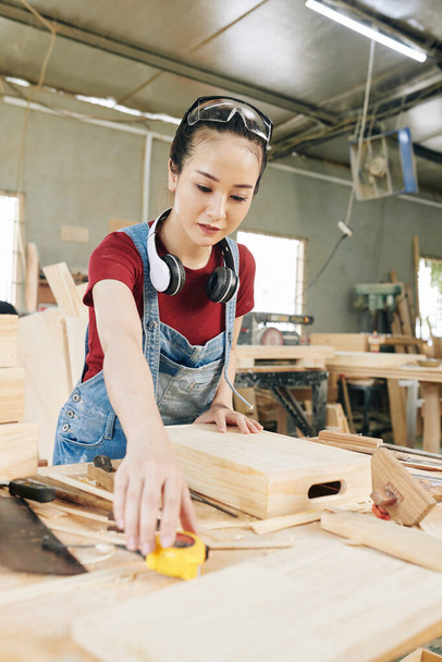Jovem carpinteiro asiático feminino medindo gaveta de madeira que ela fez com fita métrica - Foto, Imagem