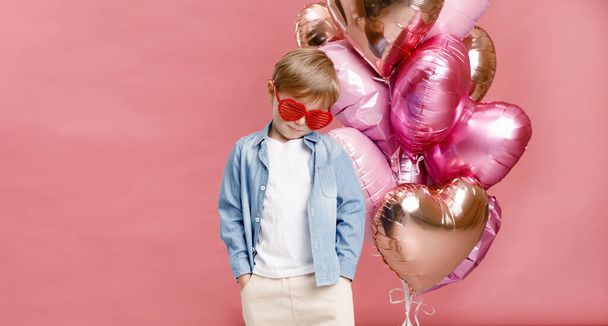 Boy dancing, smiling and having fun near  big branch of pink heart-shaped ballons. Isolated on pink background. - Foto, Imagen