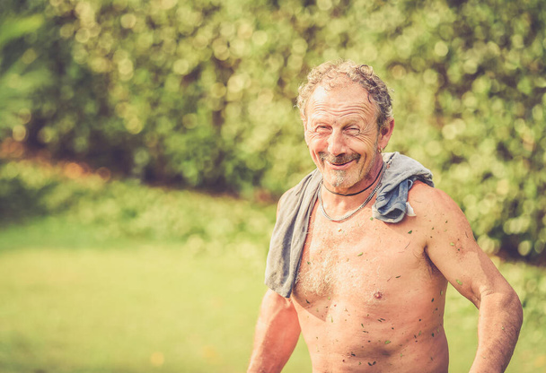 Portrait of smiling shirtless gardener in front of green plants in the garden. - Photo, Image