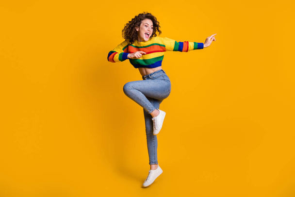 Full length photo of jumping lady wearing casual colorful sweater dancing pointing looking empty space standing one leg isolated yellow color background - Fotografie, Obrázek
