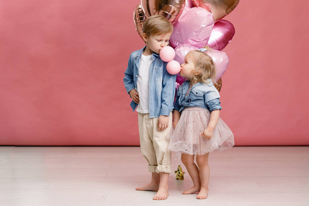 Little boy and girl hugging, dancing, smiling and having fun near big branch of pink heart-shaped ballons. Valentins day concept. Isolated on pink background. - Photo, Image