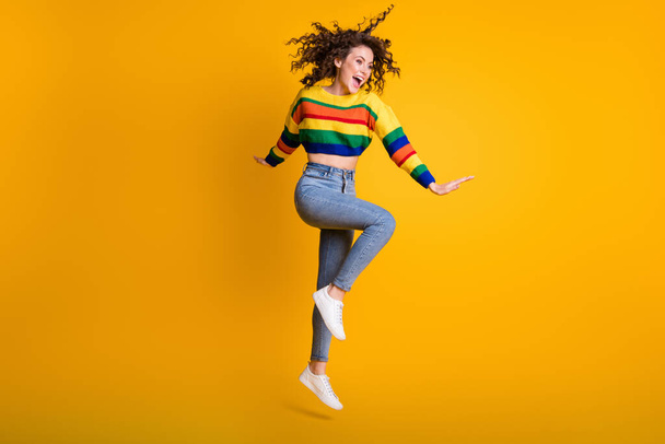 Full length photo of funny jumping woman dressed casual colorful sweatshirt looking empty space isolated yellow color background - Фото, изображение
