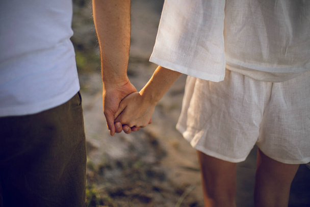 ζευγάρι στην αγάπη κρατώντας τα χέρια και περπατώντας στην παραλία στο ηλιοβασίλεμα - Φωτογραφία, εικόνα