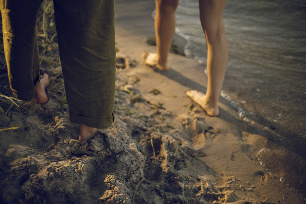 Ayaklarını kumsala koy. Ayaklar kumun üzerinde, suyun yanında. Nehir kenarında aşık bir çift. - Fotoğraf, Görsel