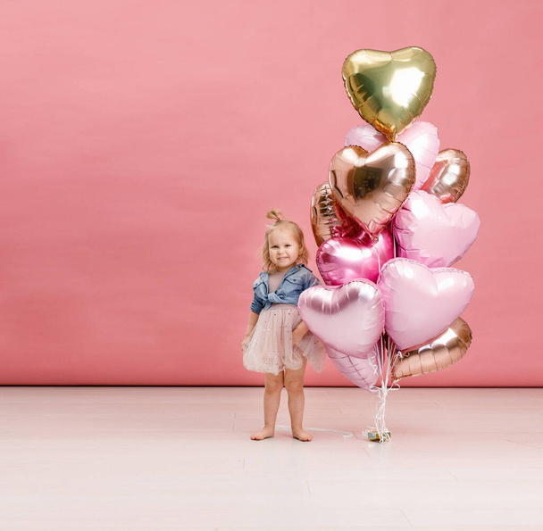 Cute little girl dancing, smiling and having fun near big branch of pink heart-shaped ballons. Isolated on pink background. - Fotografie, Obrázek