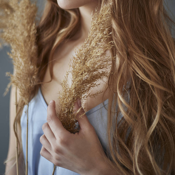 Woman with long wavy blond hair holds dry reeds in her hands - Photo, Image