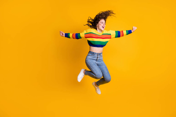 Full length photo of jumping lady wearing casual colorful sweater hands arms side closed eyes isolated yellow color background - Фото, изображение