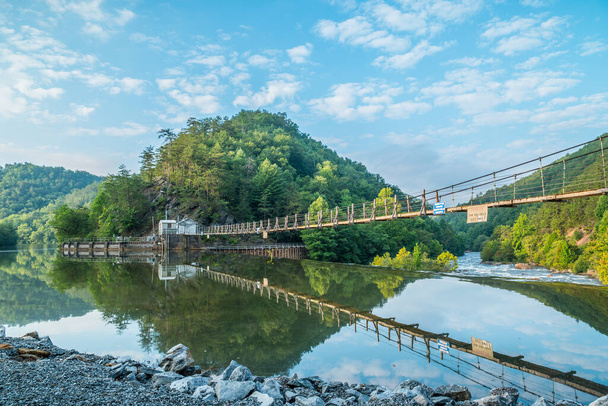 A wide angle view of the powerhouse against the mountain and maintenance bridge reflecting in the Ocoee river flowing whitewater downstream in the background on a bright sunny day in late summertime - Photo, Image
