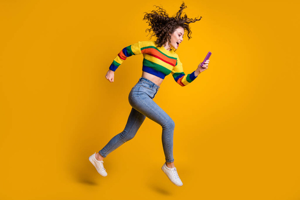 Profile full size photo of cheerful pretty wavy hair girl run read message wear sweater jeans sneakers isolated on yellow background - Valokuva, kuva