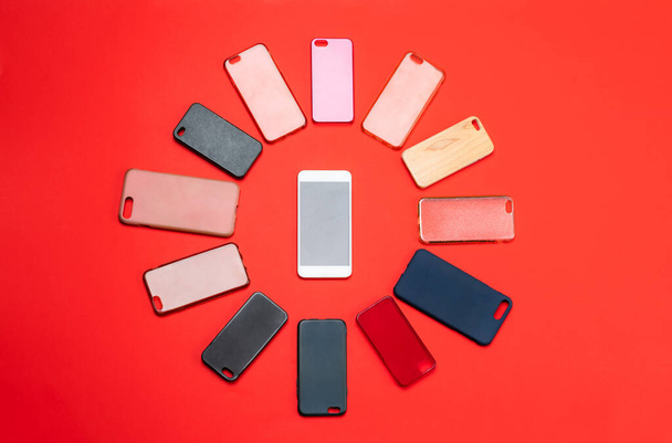 Elección de cubiertas traseras de plástico multicolor para teléfonos móviles en fondo rojo con un teléfono inteligente en el lateral - Foto, imagen