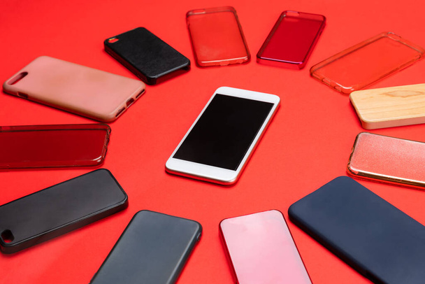 Вибір різнокольорових пластикових обкладинок для мобільних телефонів на червоному тлі з смартфоном збоку
 - Фото, зображення