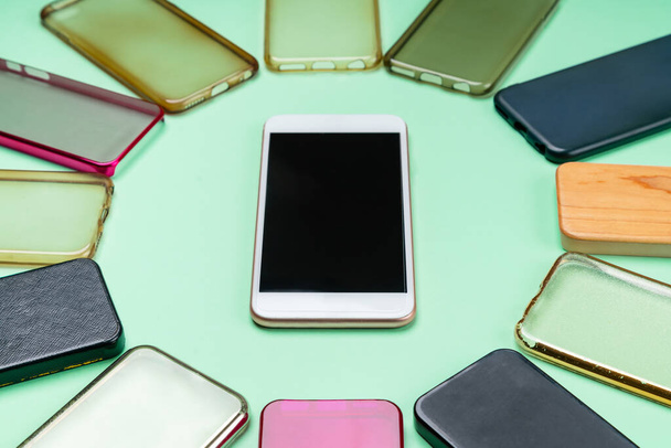 Choice of multicolored plastic back covers for mobile phones on green background with a smart phone on the side - 写真・画像