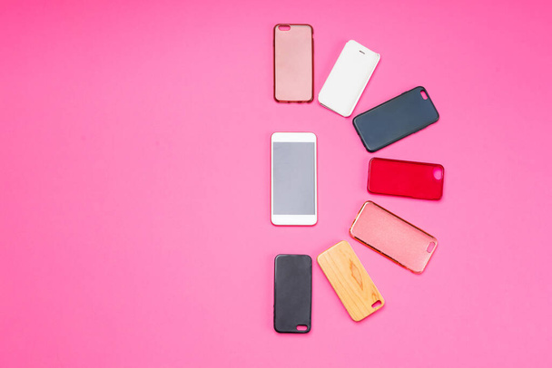 Keuze uit veelkleurige plastic achterkant voor mobiele telefoons op roze achtergrond met een smartphone aan de zijkant - Foto, afbeelding