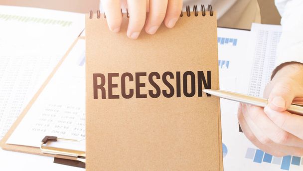 Tekst recessie op bruin papier notitieblok in zakenman handen op de tafel met diagram. Bedrijfsconcept - Foto, afbeelding