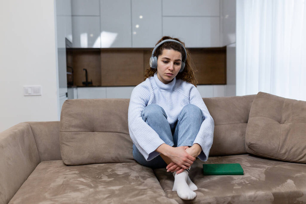 Mujer hermosa joven está descansando en casa, sentado en el sofá, y escuchar música en los auriculares - Foto, Imagen