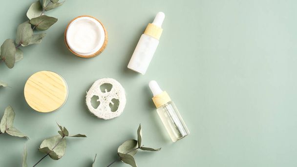 Set of herbal cosmetic and eucalyptus leaves on green background. Jar of moisturizer cream, facial serum, loofah. Natural organic beauty products. - Fotó, kép